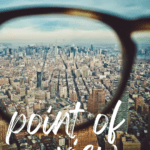 A person holds up a set of tortoise shell glasses that look over the city